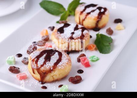 Crêpes au fromage cottage avec raisins secs, fruits confits et chocolat sur une assiette blanche, vue du dessus Banque D'Images