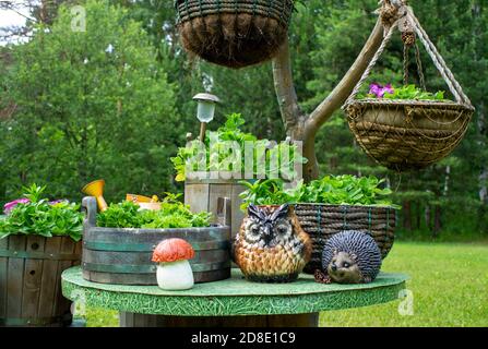 Pots de fleurs suspendus faits à la main et pots de pétunia en bois dans le jardin d'été. Figurines décoratives d'un hibou, d'un hérisson et d'un champignon sur la table. ECO desi Banque D'Images