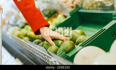 Au supermarché: Gros plan photo de la main de la femme prenant l'avocat de la section des produits frais et le place dans le panier. Banque D'Images