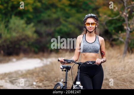 S'adapter à une jeune femme portant des vêtements de sport debout avec sa bicyclette arrière-plan d'automne flou le jour de l'automne Banque D'Images