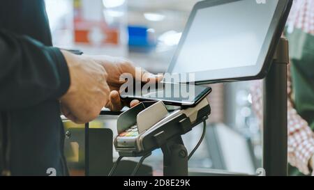 Dans le supermarché gros plan de l'homme payant avec un smartphone au comptoir caisse. Utilisation du système de paiement NFC sans fil moderne et pratique Banque D'Images