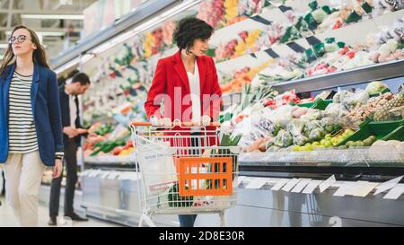 Au supermarché: Belle jeune femme marche à travers la section des produits frais, choisit des légumes. Le client recherche des fruits et légumes au Banque D'Images