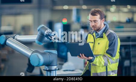 En usine : l'ingénieur en automatisation utilise un ordinateur portable pour programmer le bras robotique. Nouvelle ère dans l'industrie de la fabrication automatique. Banque D'Images