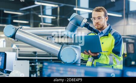 En usine : l'ingénieur en automatisation utilise un ordinateur portable pour programmer le bras robotique. Nouvelle ère dans l'industrie de la fabrication automatique. Banque D'Images