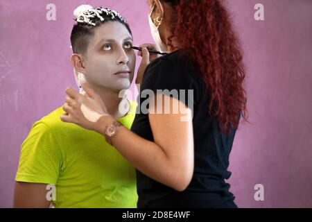 Maquilleuse avec un masque pour peindre le visage d'un homme halloween Banque D'Images