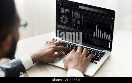 Homme d'affaires noir travaillant sur un ordinateur portable avec des graphiques assis au bureau Banque D'Images