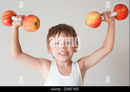 fort petit caucasien drôle enfant dans blanc tank top soulever deux haltères de pomme Banque D'Images