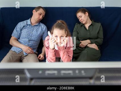 Pré-adolescente avec sommeil regarder la télévision la nuit pendant que ses parents dorment sur le canapé, famille à la maison Banque D'Images