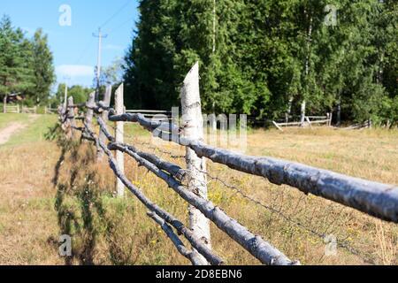 Clôture rurale en bois avec fil barbelé, l'herbe sèche est sur un champ en été Banque D'Images