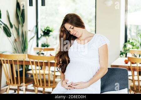 Jolie jeune femme enceinte à tête rouge à l'estime en robe blanche. Banque D'Images