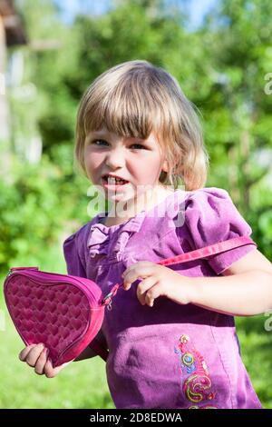 Portrait d'une jeune fille caucasienne soulignant avec un petit sac rose dans ses mains, portant la robe dans le jardin d'été, lookiong à l'appareil photo Banque D'Images