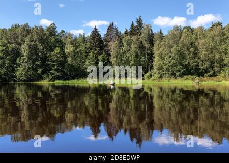 Pêcheur solitaire qui attrape le poisson du bateau en bois au milieu de la forêt de la baie du lac, eau calme à l'heure de la journée Banque D'Images