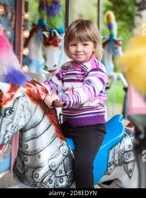 Adorable petite fille à cheval sur un cheval manège à la foire ou au marché, en plein air. Joyeux enfant caucasien s'amuser Banque D'Images