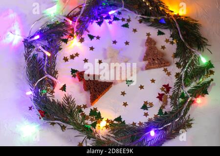 Fond de Noël ou de fête du nouvel an. Composition de cartes de voeux avec couronne verte, guirlande lumineuse colorée, paillettes et sapins faits de pain. Banque D'Images