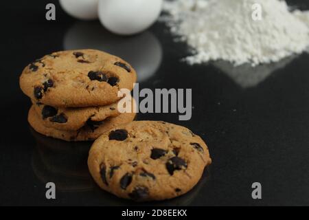 cuisine encore la vie processus de cuisson biscuits au chocolat faits maison avec du chocolat des gouttes dans la farine de fond et des oeufs de poulet se trouvent sur un miroir noir à l'arrière Banque D'Images