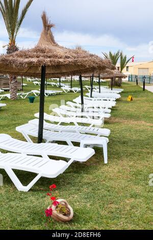 Des chaises longues en plastique vides sous des parasols sont sur un pré vert dans une zone d'hôtel, la saison annulée en raison du coronavirus Banque D'Images