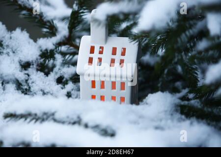 Maison de lanternes en céramique avec bougie sur branches de sapin couvertes de neige dans le parc d'hiver. Banque D'Images