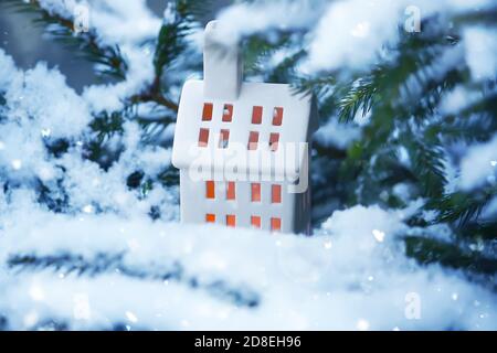 Maison de lanternes en céramique avec bougie sur branches de sapin couvertes de neige dans le parc d'hiver. Banque D'Images