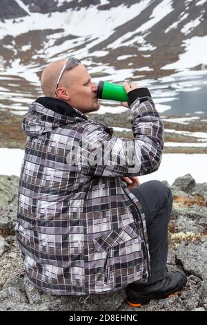 Homme caucasien buvant de l'énergie sur le sommet de la montagne, un grimpeur ou alpiniste assis sur le rocher Banque D'Images