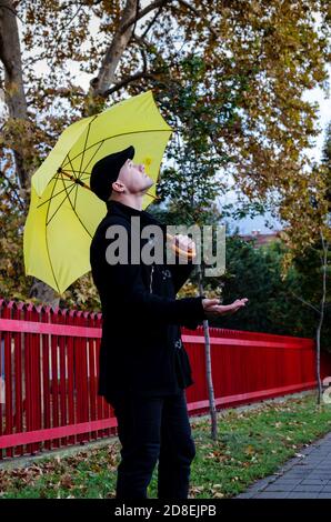 Homme en manteau noir, debout dans les rues de la ville sous le parapluie jaune vérifiant avec la paume de sa main si la pluie avait cessé de tomber. Prévisions. Banque D'Images