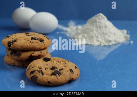 cuisine processus de cuisson biscuits au chocolat faits maison avec des gouttes de chocolat la farine de fond et les œufs de poulet se trouvent sur un bleu miroir arrière brillant Banque D'Images