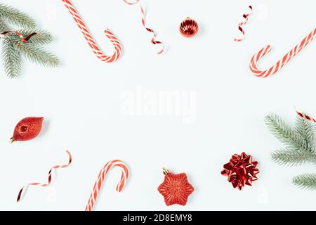 Cadre plat de Noël avec Cannes en sucre, branches d'arbre de noël et boules rouges traditionnelles sur fond blanc Banque D'Images