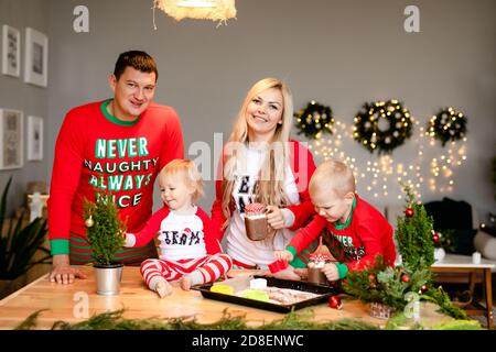 Une famille heureuse de quatre parents, papa, fils et petite fille boivent du cacao de Noël dans la cuisine. Banque D'Images