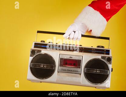 Main du Père Noël tenant un lecteur de radio cassette sur un arrière-plan jaune Banque D'Images