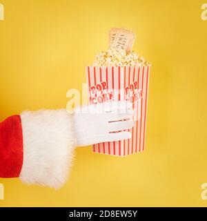 Main du Père Noël tenant un seau rouge et blanc avec pop-corn sur fond jaune Banque D'Images