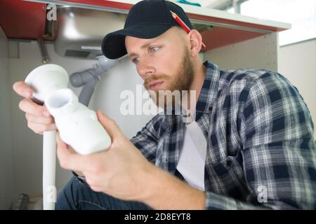 l'homme répare quelque chose à l'intérieur de l'armoire de cuisine sous l'évier Banque D'Images