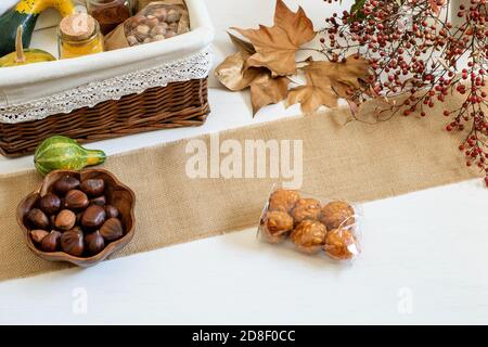 Citrouilles, épices et noisettes emballées dans un panier cadeau artisanal. Châtaignes et panelles de piñones sur la table rustique blanche. Halloween festive Emotions, c Banque D'Images