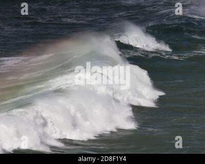 Vagues de rupture avec un arc-en-ciel dans le jet balayé par le vent. Près de la plage de Poldhu, Poldhu Cove, Cornwall. Une crique populaire pour les surfeurs et les débutants de surf. Banque D'Images