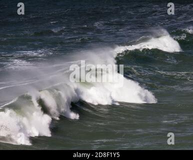 Vagues de rupture pulvérisation balayée par le vent. Près de la plage de Poldhu, Poldhu Cove, Cornwall. Une crique populaire pour les surfeurs et les débutants de surf. Banque D'Images