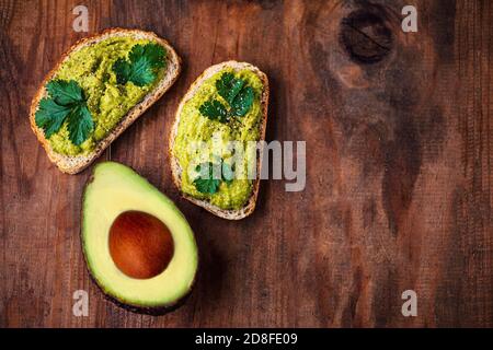 Moitié d'aocado sur une ancienne table en bois, espace de copie. Sandwich à l'avocat sur du pain de seigle sombre vue de dessus. Banque D'Images