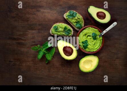 Avocat sur fond en bois sombre. Sauce guacamole avec pain grillé à l'avocat, menthe et herbes. Vue de dessus. Copier l'espace Banque D'Images