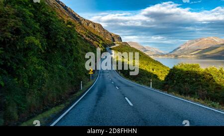 Autoroute longue et sinueuse sur le bord de l'étourdissement lac Wakatipu près de Queenstown bordé par les Alpes du Sud Banque D'Images