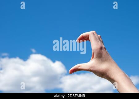 Gros plan d'un geste de la main en forme de demi-cœur contre les nuages et le ciel bleu. Le concept de solitude, d'amour. Copier l'espace Banque D'Images