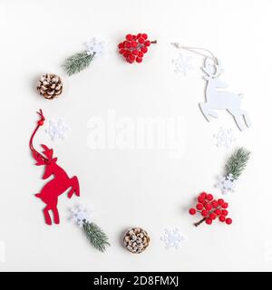 Décorations de Noël : cerf, brindilles de sapin, baies rouges, flocons de neige disposés en cercle sur blanc. Copier l'espace pour le texte. Banque D'Images