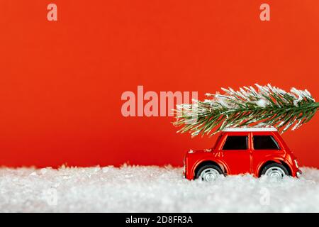 Petite voiture de jouet rouge transportant un arbre de spruse sur une route enneigée. Carte de vœux de Noël festif Banque D'Images