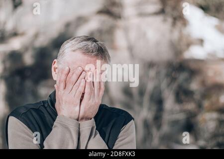 Portrait d'un homme d'âge moyen dans la rue, couvrant son visage avec ses mains. Expression de tristesse, de doute, de désespoir. Concept de crise. Copier l'espace. Banque D'Images