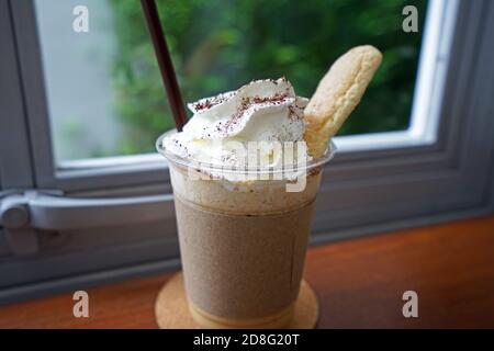 Gros plan sur une tasse de smoothies au latte à café à emporter sur le dessus avec de la crème fouettée et du pain court servi dessus plateau en bois Banque D'Images