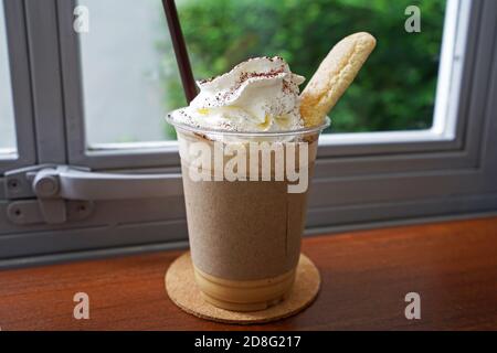 Gros plan sur une tasse de smoothies au latte à café à emporter sur le dessus avec de la crème fouettée et du pain court servi dessus plateau en bois Banque D'Images