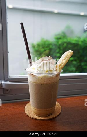 Gros plan sur une tasse de smoothies au latte à café à emporter sur le dessus avec de la crème fouettée et du pain court servi dessus plateau en bois Banque D'Images