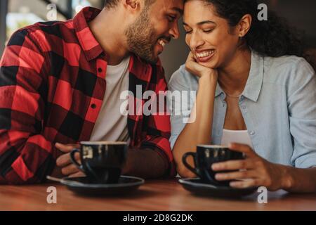 Couple affectueux prenant un café dans un café. Couple aimant assis au café en touchant les fronts et en souriant. Banque D'Images