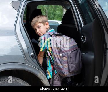 Portrait d'un garçon souriant avec sac d'école qui se perd dans la voiture. Prendre un élève après l'école. Le garçon entre dans la voiture Banque D'Images