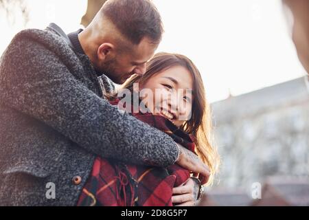 Heureux couple multiracial réchauffant par le tissu écossais rouge ensemble à l'extérieur dans la ville Banque D'Images