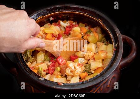 Gros plan à la main mélange un ragoût de légumes dans une casserole avec une cuillère en bois. Alimentation nationale. Concept d'alimentation saine Banque D'Images