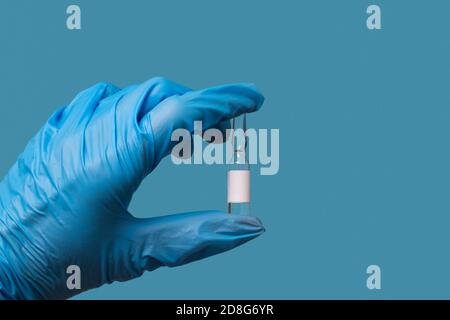 Une main de médecin dans un gant bleu tient une bouteille De COVID-19 médicament ou vaccin sur fond bleu Banque D'Images