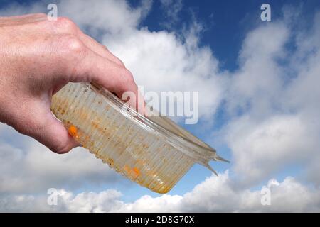 Une main femelle tient un récipient en plastique sale pour les aliments produits sur le fond d'un ciel bleu avec des nuages Banque D'Images