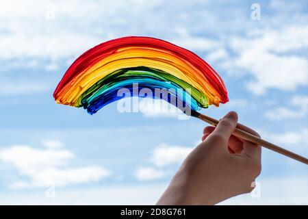 La brosse à main en gros plan peint un arc-en-ciel sur le ciel de la fenêtre, les nuages, la fin de la quarantaine, l'auto-isolement Banque D'Images
